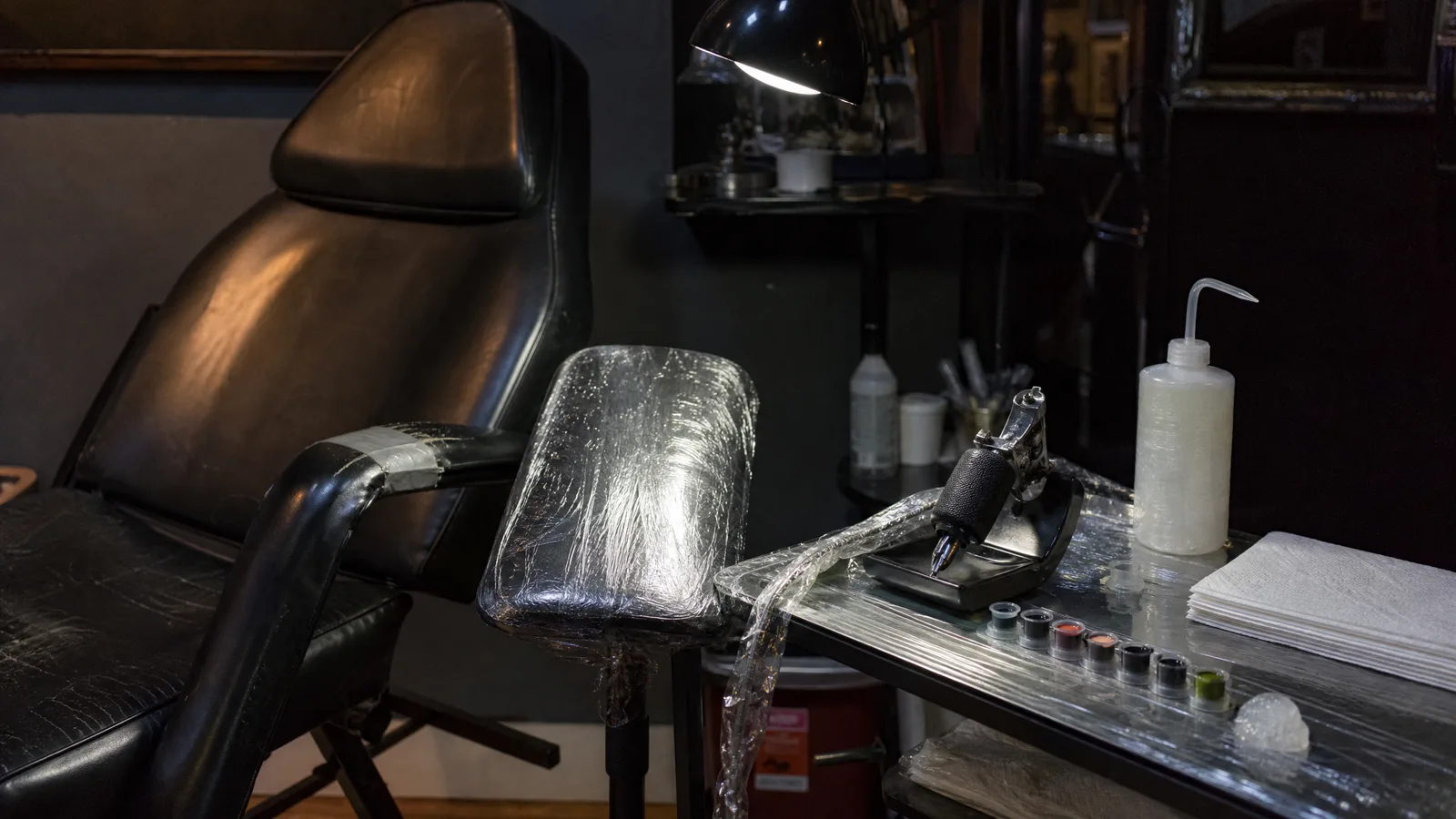 Tattoo station with a machine on a stand, ink caps in a tray and barrier film wrapped over the armrest